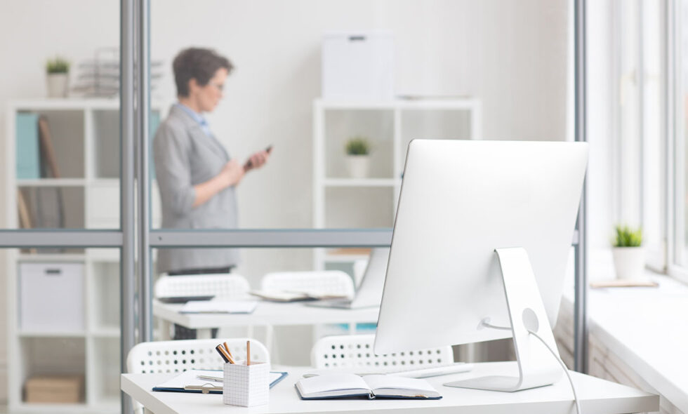 Workplace of employee by transparent board with office worker behind